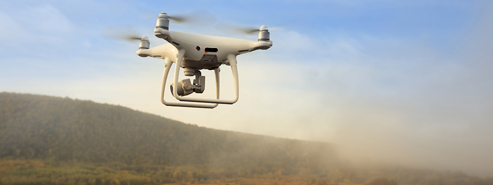 A drone flies through the air above an outback scene.